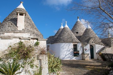 Fototapeta na wymiar Group of Trulli with garden, traditional old houses and old stone wall in Puglia, Italy, Europe