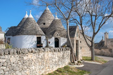 Fototapeta na wymiar Group of Trulli with garden, traditional old houses and old stone wall in Puglia, Italy, Europe