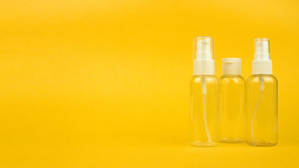 Empty cosmetic plastic bottles with pump and spray on yellow background with copy space. Clear cosmetic containers kit for travel. Banner template, mockup for advertising, social media. Stock photo.