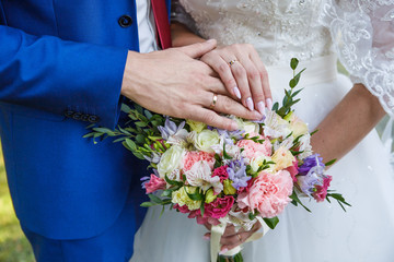 Hands of newlyweds with wedding rings and a bouquet of flowers. The groom in a blue suit and red tie. The concept of wedding love and Valentine's day