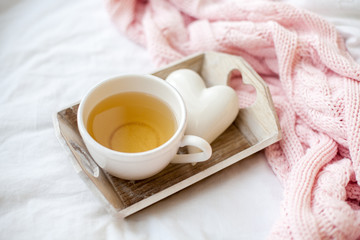 Obraz na płótnie Canvas Beautiful white cup with tea on the bed, pink knitted plaid, decor Valentine's Day. Breakfast in bed. Morning. Spring. Cozy.