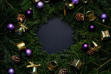 Fototapeta na wymiar Christmas wreath decorated with purple and gold toys with a black background in the middle