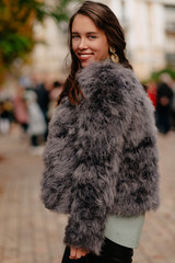 Attractive smiling european woman with dark wavy hair wearing stylish fur coat walking in the city in good day