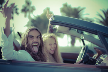 Happy young couple having fun inside convertible sport car. Couple listening to rock music. Vacation, journey and relationship concept. Focus on man face - Image