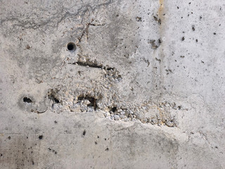 Concrete surface with caverns and exposed gravel stones and reinforcement rebars