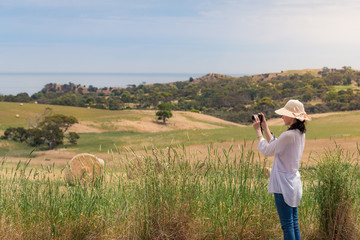 Woman tourist taking photos of countryside landscape with straw bales on field
