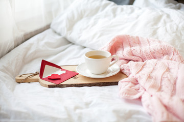 Obraz na płótnie Canvas Beautiful white cup with tea on the bed, pink knitted plaid, postcard Happy Valentine's Day. Breakfast in bed. Morning. Spring. Cozy.