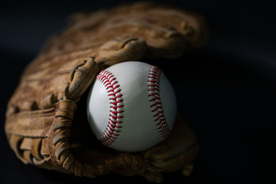 Baseball in a glove on black background.