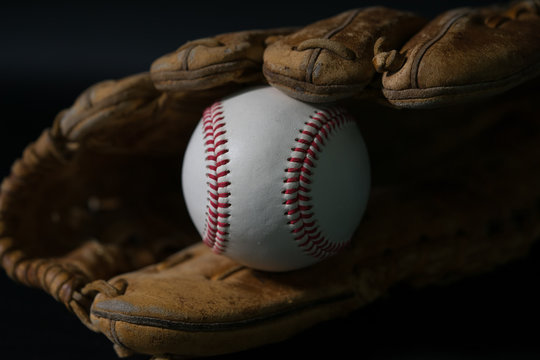 Baseball in a glove on black background.