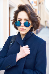 Summer sunny lifestyle fashion portrait of young stylish hipster woman walking on the street