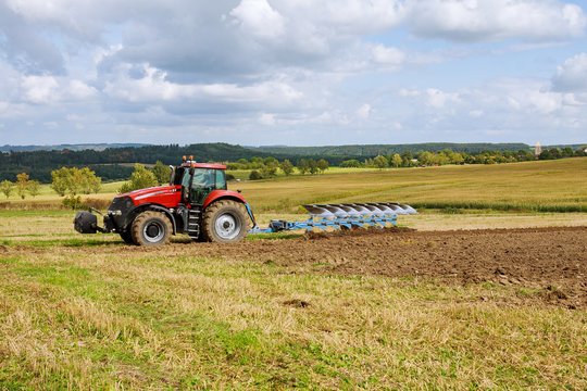 Farmer in red tractor preparing land with plow for sowing