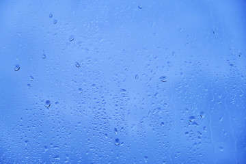 Glass background with big drops of rain. Autumn window with the texture of water drops against a cloudy blue sky
