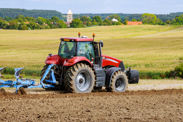 Obraz premium Farmer in red tractor preparing land with plow for sowing