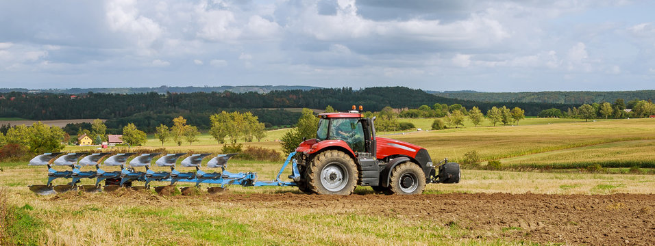 Fototapeta Farmer in red tractor preparing land with plow for sowing