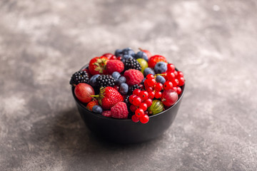 Black bowl with fresh summer berries on a gray background.