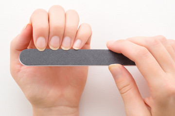 Woman hands using black nail file on white table background. Closeup. Point of view shot.
