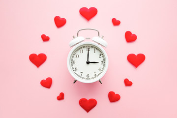 Bright red hearts around white alarm clock on pastel pink background. Dating time. Love concept. Closeup.