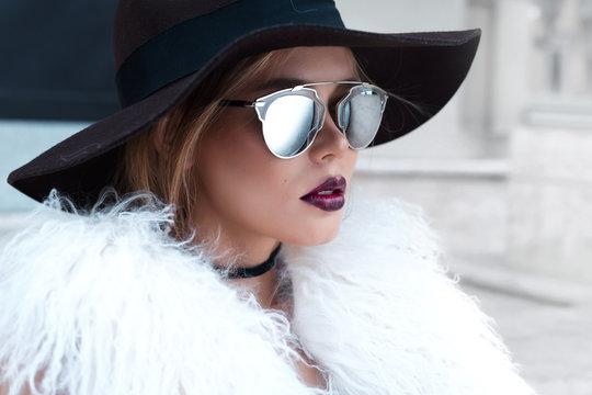 Closeup portrait of young beautiful fashionable woman with sunglasses. Lady posing on dark grey background. Model wearing stylish wide-brimmed hat, jacket. Girl looking at camera. Female fashion.Toned