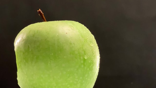 Closeup of rotating bitten apple in the studio with a black backdrop. Fresh bite into a green apple. Bitten sweet apple 
with white core rotating.