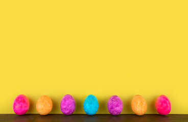 multi-colored painted easter eggs stand on a brown wooden table on a yellow background. Place for text