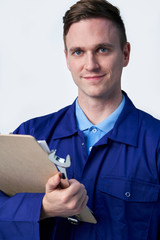 Studio Portrait Of Male Engineer With Clipboard And Spanner Against White Background