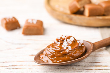 Salted caramel in spoon on white wooden table, closeup