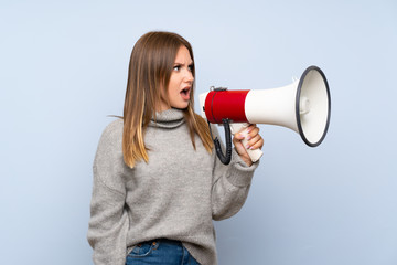 Teenager girl with sweater over isolated blue background shouting through a megaphone