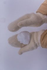 Woman makes a snowball in the hands of white mittens