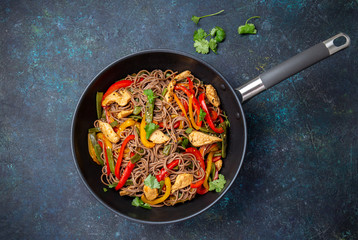 Japanese dish buckwheat soba noodles with chicken and vegetables carrot, bell pepper and green beans in wok on dark blue background