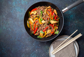 Japanese dish buckwheat soba noodles with chicken and vegetables carrot, bell pepper and green beans in wok on dark blue background
