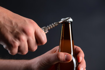 Men opening cold bottle of beer with cap on black background. Hands cracking refrigerated wheat or...
