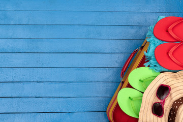 Suitcase with flip-flops, hat and sunglasses on wooden table.
