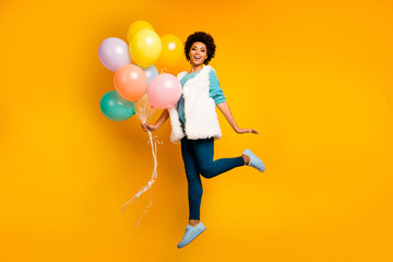 Fototapeta na wymiar Fulll body photo of funny afro american girl hipster jump enjoy autumn holiday hold baloons wear stylish white turquoise teal pullover blue trousers isolated bright color background