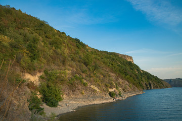 summer time nature reservation landscape of green hill coast of lake water shoreline with blue sky background