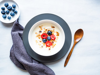 Müsli mit Joghurt, Himbeeren und Blaubeeren in einer weißen Schüssel auf einem grauen Teller, servierfertig, gesunde Ernährung