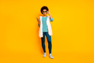 Full length photo positive afro american girl walk relax use smartphone follow comment news wear blue pants trousers turquoise sweater stylish trenyd white isolated yellow color background