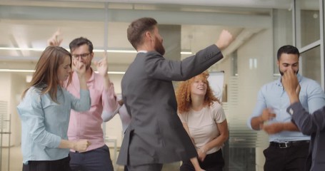 Young diverse business workers in good mood having fun together after finishing working day. Group of managers dancing, smiling and rejoicing. Concept of people, work, positive emotions.