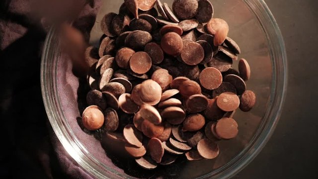 Slowmotion chocolate drops falling in a bowl, dark background top view