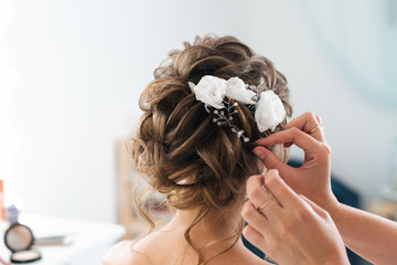 hairdresser makes an elegant hairstyle styling bride with white flowers in her hair