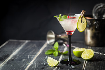 Fresh classic lime margarita cocktail with strawberry syrup over black background