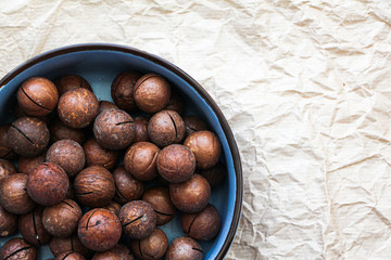 Macadamia nuts in blue ceramic bowl. Organic healthy food concept