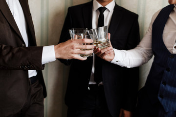 stylish friends businessmen in suits toasting with glasses of whiskey indoors, closeup. groom's morning