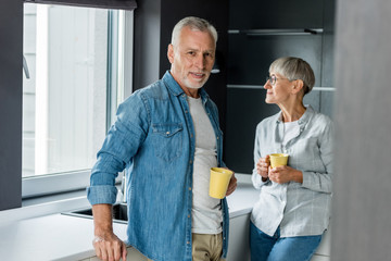 smiling man and mature woman holding cups in new house