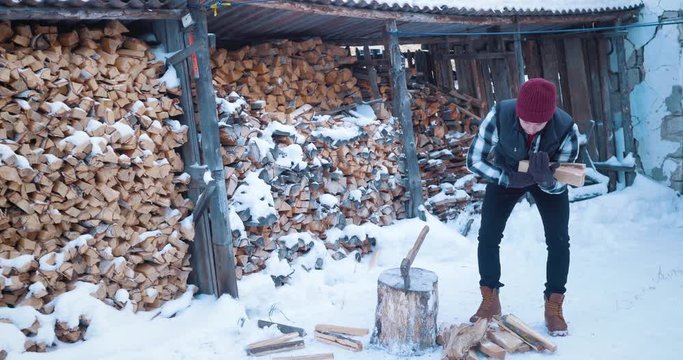 A man lumberjack in the yard in winter. Collects firewood and carries 4k.