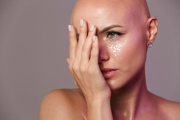 Portrait of young half-naked bald woman covering her face with hand