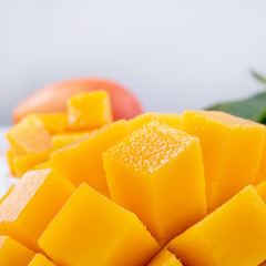 Fresh mango,beautiful chopped fruit with green leaves on bright wooden table background. Tropical fruit design concept, close up, copy space.