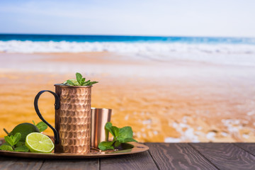 Cold Moscow Mules cocktail with ginger beer, vodka and lime over beach and seaside background