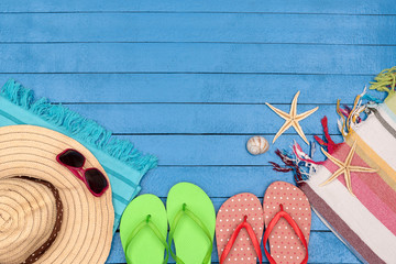 Flip-flops, hat, beach towel and sunglasses on wooden table.