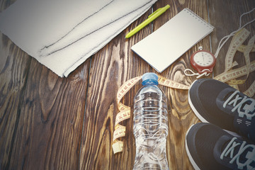 Fototapeta na wymiar Healthy lifestyle and sports background. Sports shoes, Notepad and pen, and water bottle on wooden background with copyspace, topview.