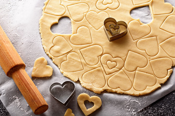 top view of cookie dough with cut out shapes in the form of heart on white parchment paper